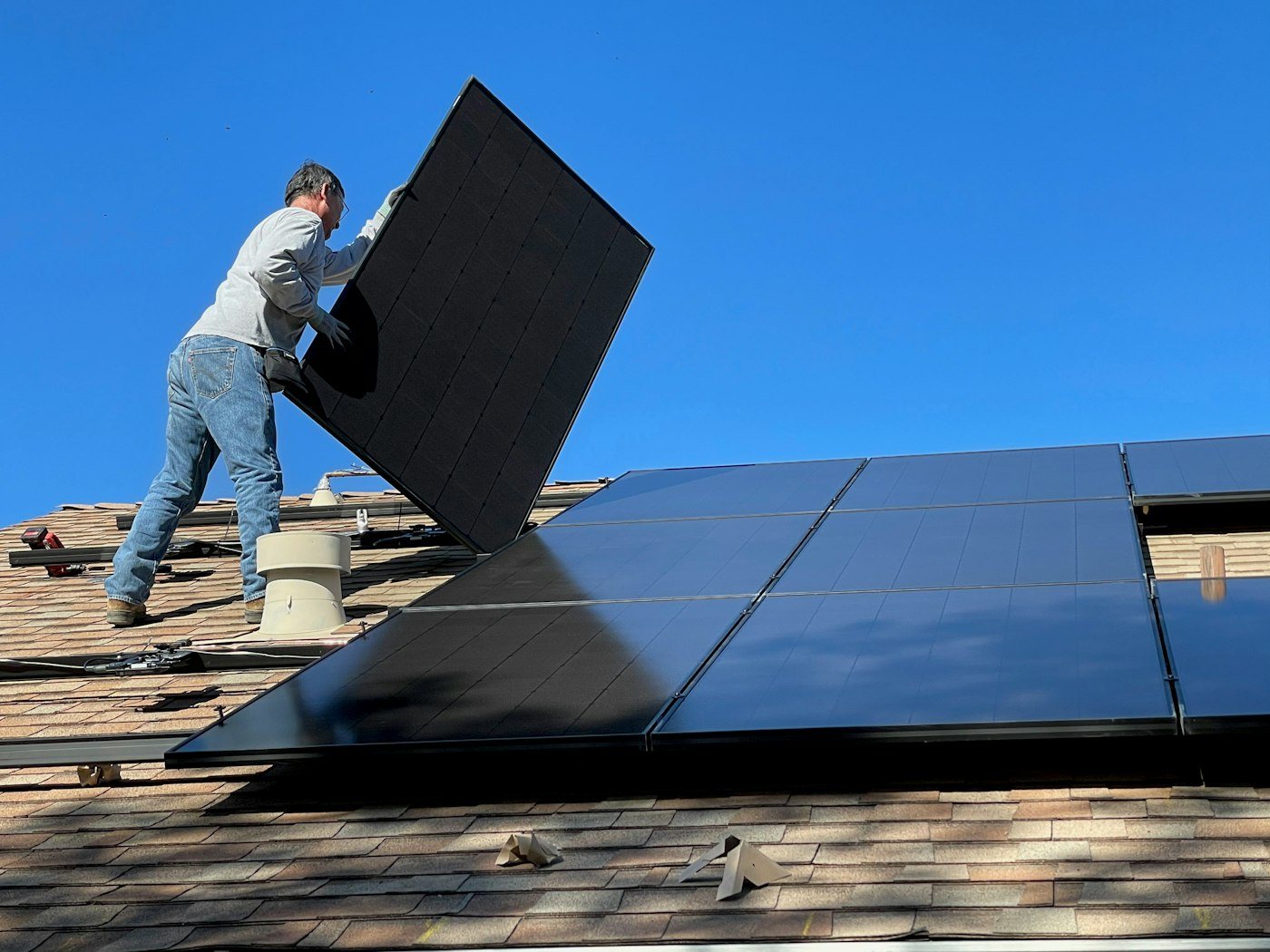 Installer placing a solar panel on a residential roof under a blue sky